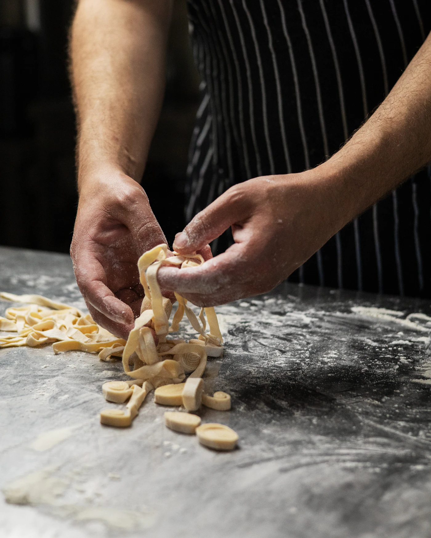 A cook's floured hands shaping fresh tagliatelle on a dark work surface