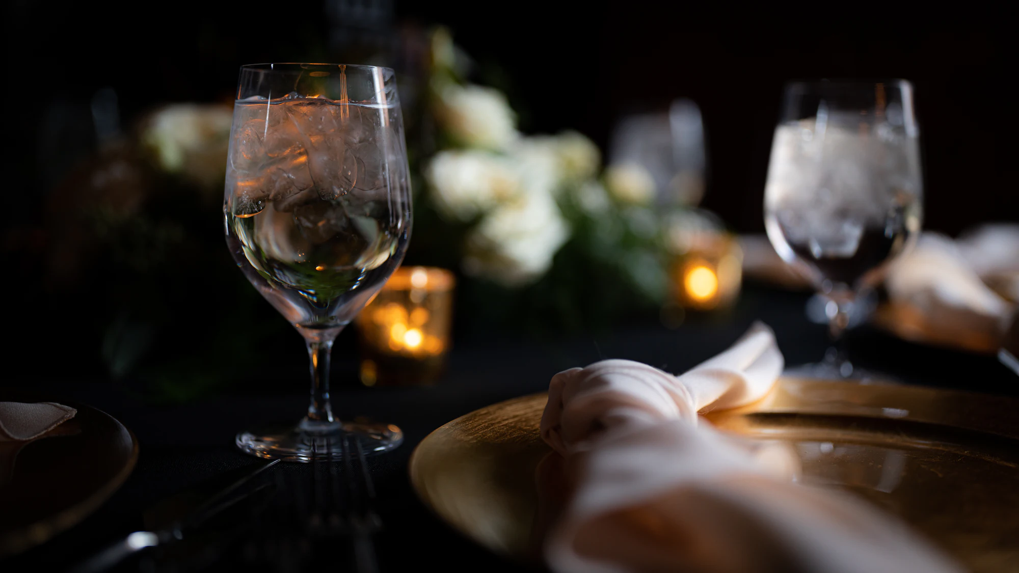 A wine glass, a folded napkin and a gold-rimmed plate on a candlelit table